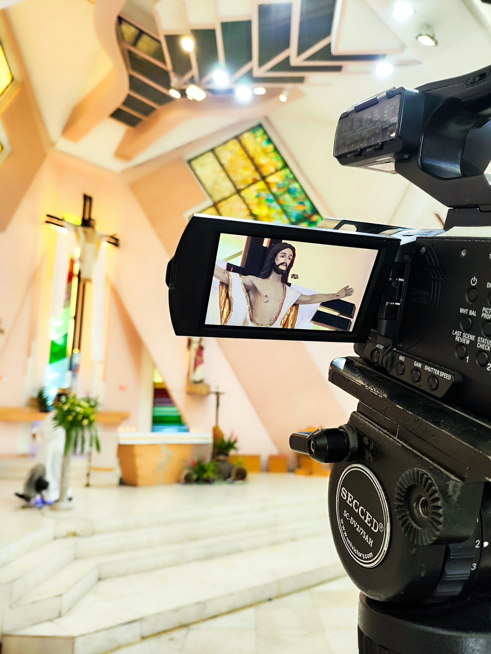 A video camera's flip-out screen framing the altar and cross at the front of a church — the kind of setup volunteers use to livestream a Sunday worship service
