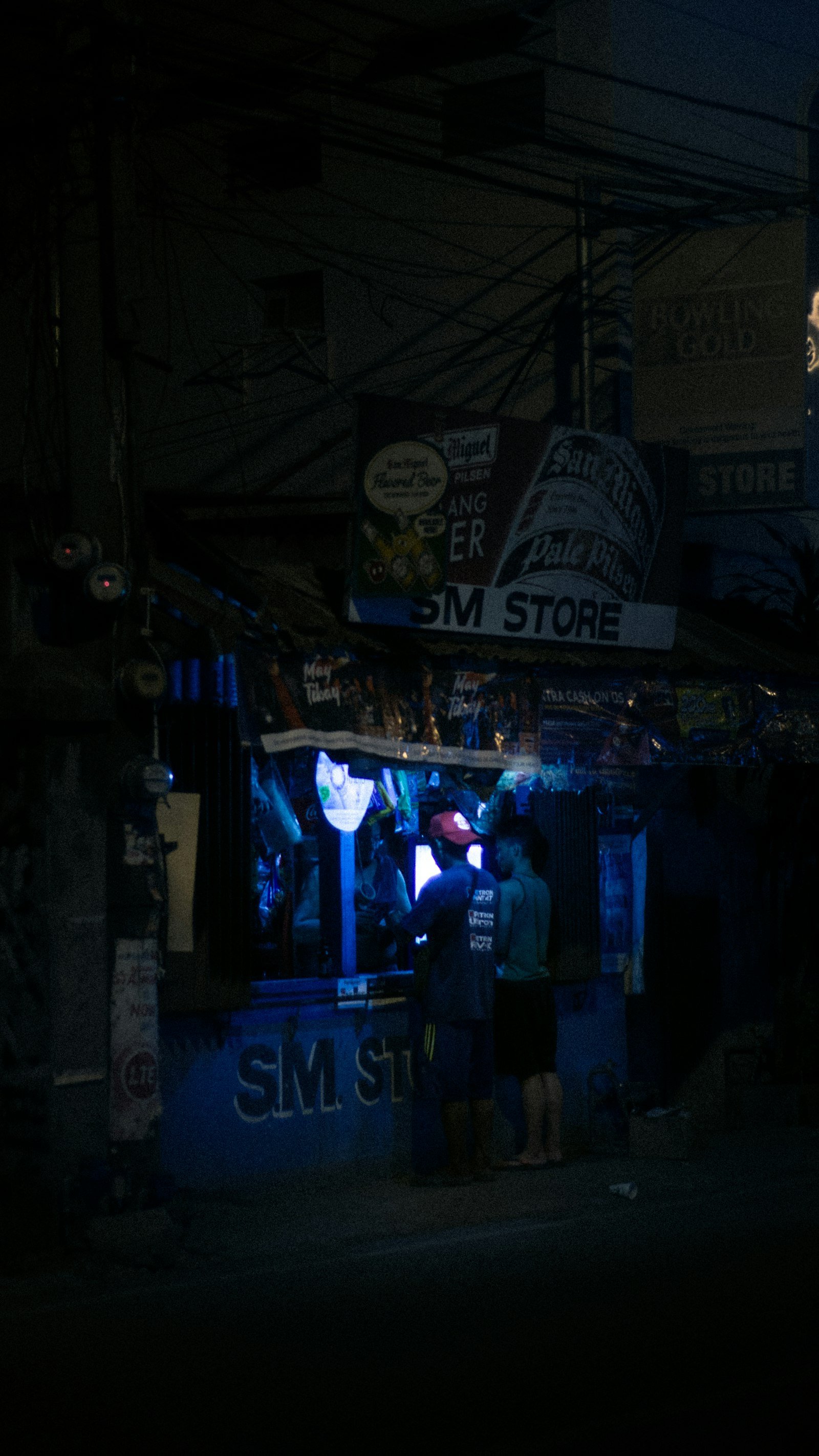 A small Filipino sari-sari store lit up in the evening with customers gathered outside — a local small business that needs to be found online